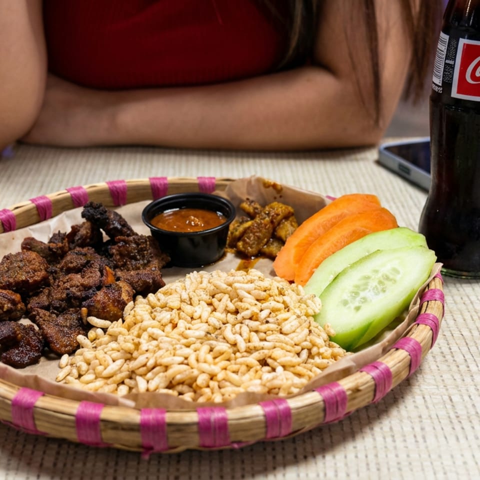 Basket of spiced fried snacks, puffed rice, sliced cucumber and carrot, dipping sauce, and Coca-Cola on a restaurant table.